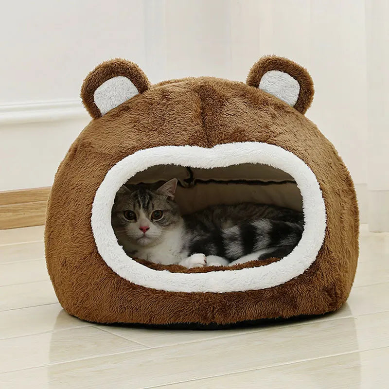 Cat lying inside a brown bear-shaped pet bed on a light wooden floor.