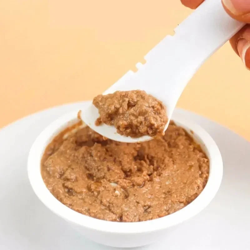 White bowl filled with brownish food, being scooped with a white spoon against a light yellow background.