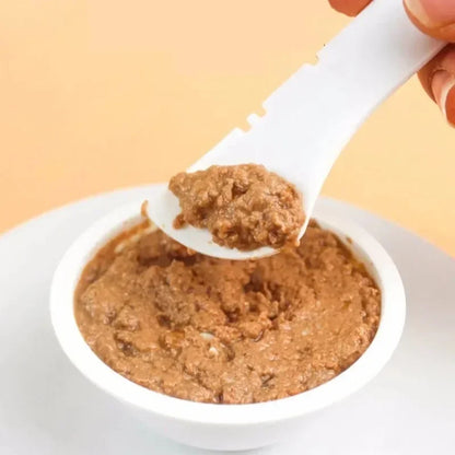 White bowl filled with brownish food, being scooped with a white spoon against a light yellow background.