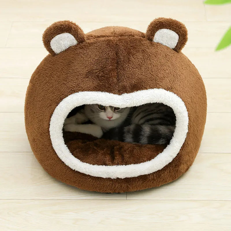 Cat peeking out from a brown bear-shaped pet bed on a light wooden floor.