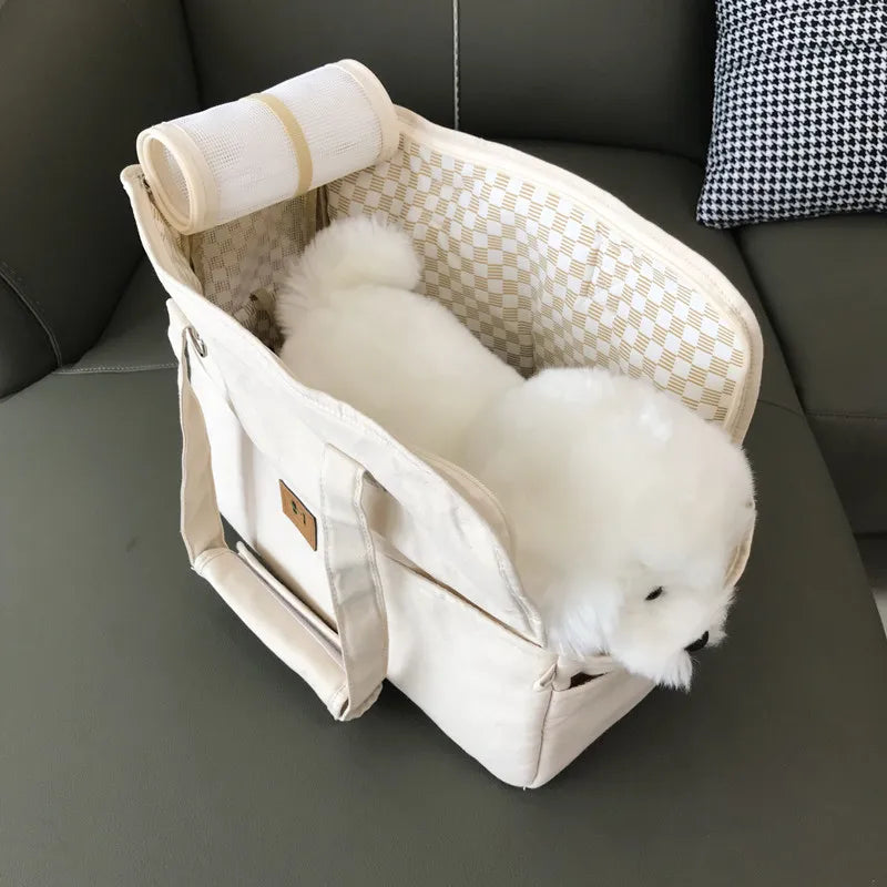 Small white dog in a beige pet carrier on a dark gray couch.