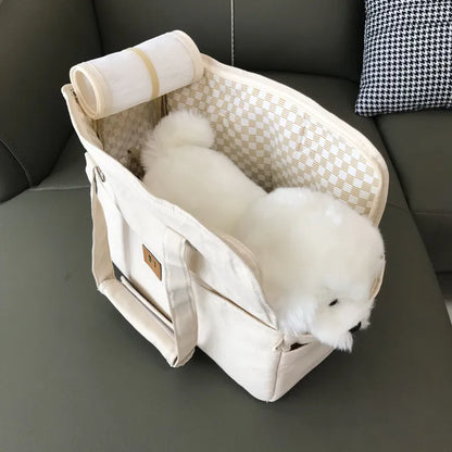 Small white dog in a beige pet carrier on a dark gray couch.