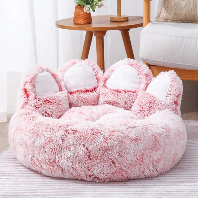Fluffy pink pet bed with cat ears on a striped surface.