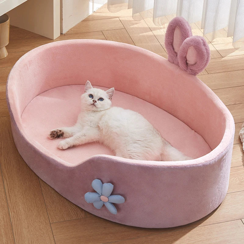 White cat lying on a pink pet bed with bunny ears and a flower design.
