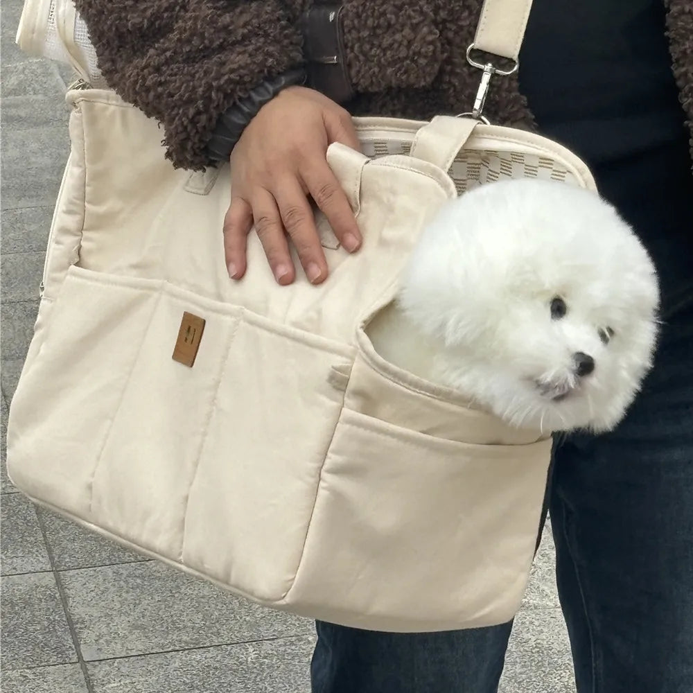 White dog peeking out from a beige pet carrier held by a person.