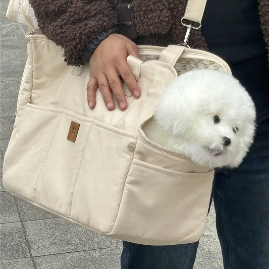 White dog peeking out from a beige pet carrier held by a person.