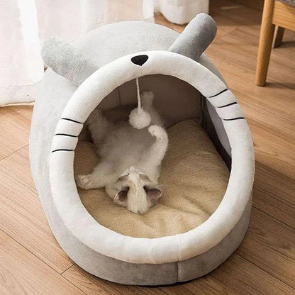 Cat playing with a toy inside a shark-shaped pet bed on a wooden floor.