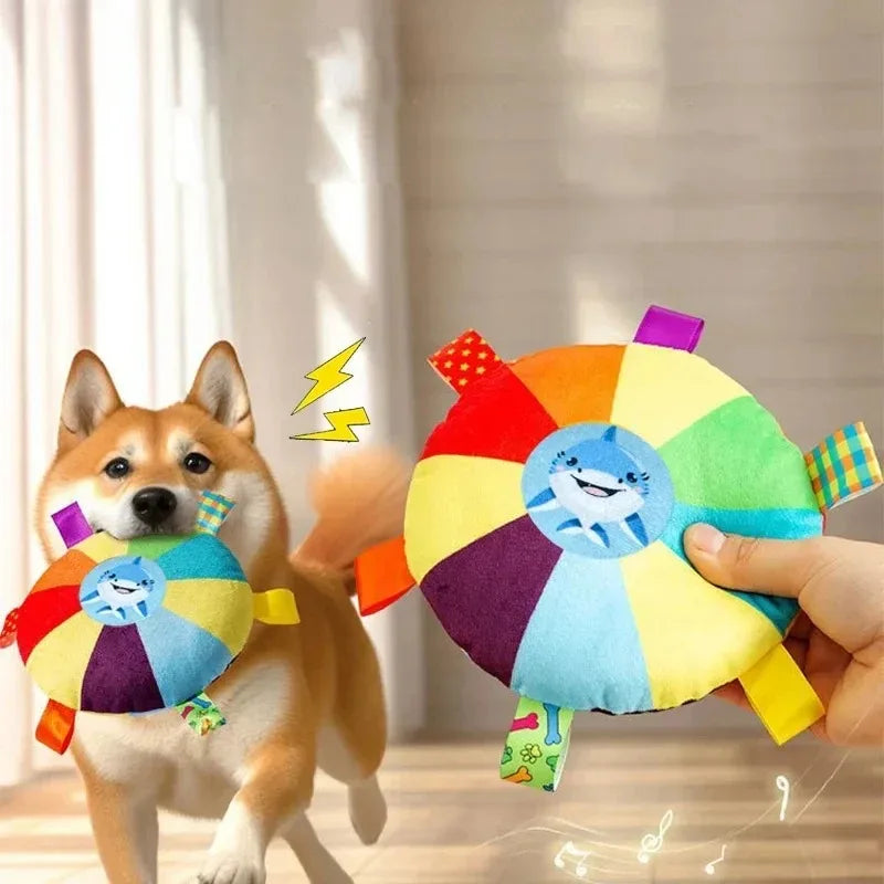 Dog playing with a colorful toy shaped like a wheel with a shark design, held by a hand.