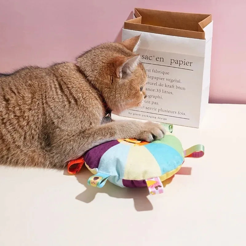 Cat playing with a colorful toy next to a paper bag on a pink background