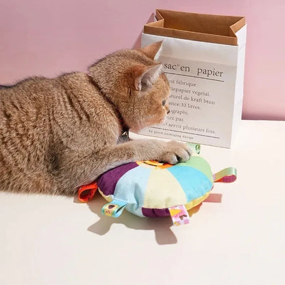 Cat playing with a colorful toy next to a paper bag on a pink background