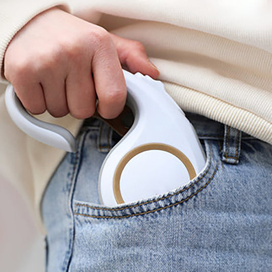 Hand holding a white handheld steamer over jeans